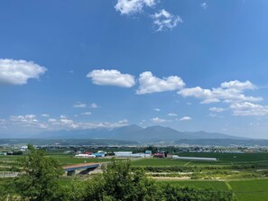 A rural landscape with fields, a bridge, and distant mountains. - GENYA Furano (Nakafurano)