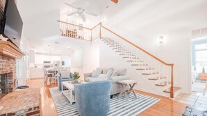 A spacious living area with a fireplace, a staircase, and a dining area in the background.