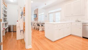 A modern kitchen with white cabinetry, a central island, and a dining area with white chairs.
