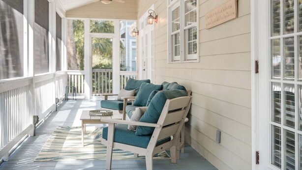 A covered porch with a ceiling fan, white railings, and a seating area with a table and chairs.