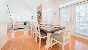 A dining area with a wooden table, white chairs, a brick fireplace, and a TV mounted on the wall.
