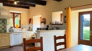 Une cuisine avec des poutres en bois, une table à manger avec des chaises et une vue sur l’extérieur.