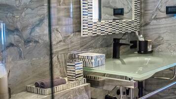 A bathroom with a glass sink, marble walls, a checkered mirror, and a towel rack with neatly rolled towels.