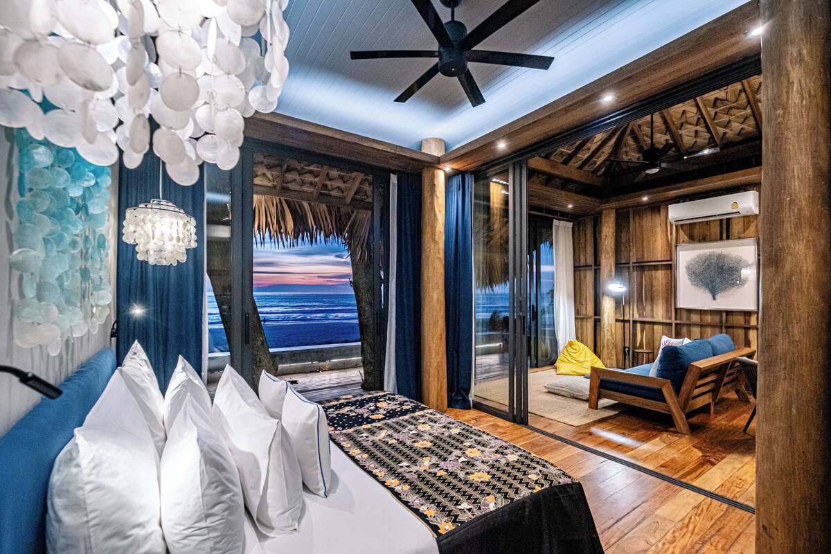 A modern bedroom with a large bed, a ceiling fan, and a view of the ocean.