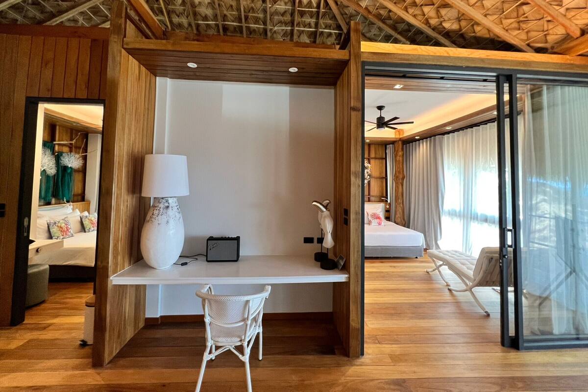 A modern bedroom with a wooden ceiling, a desk with a chair, a bed, and a large window with curtains.