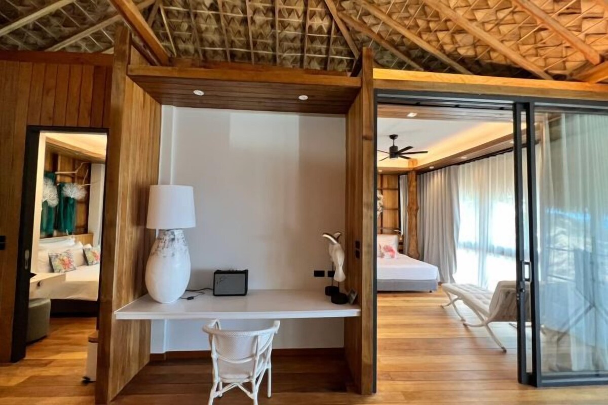 Una habitación moderna con techo de madera, un escritorio blanco con lámpara, una silla y una cama.
