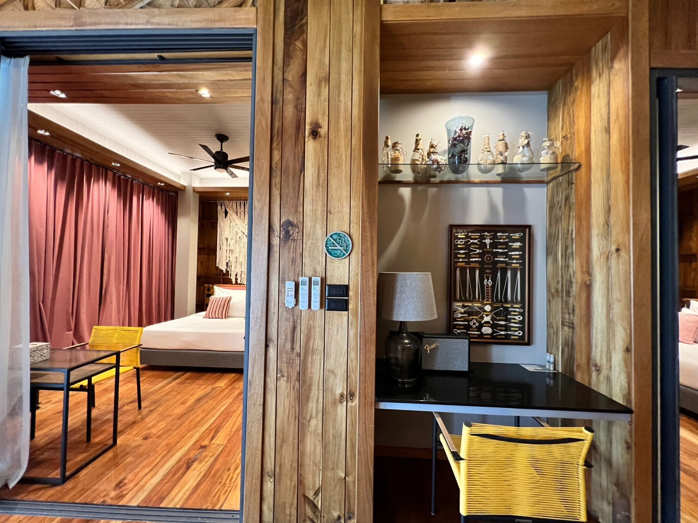 A room with a bed, a desk, a chair, a ceiling fan, and a wall-mounted shelf with decorative items.