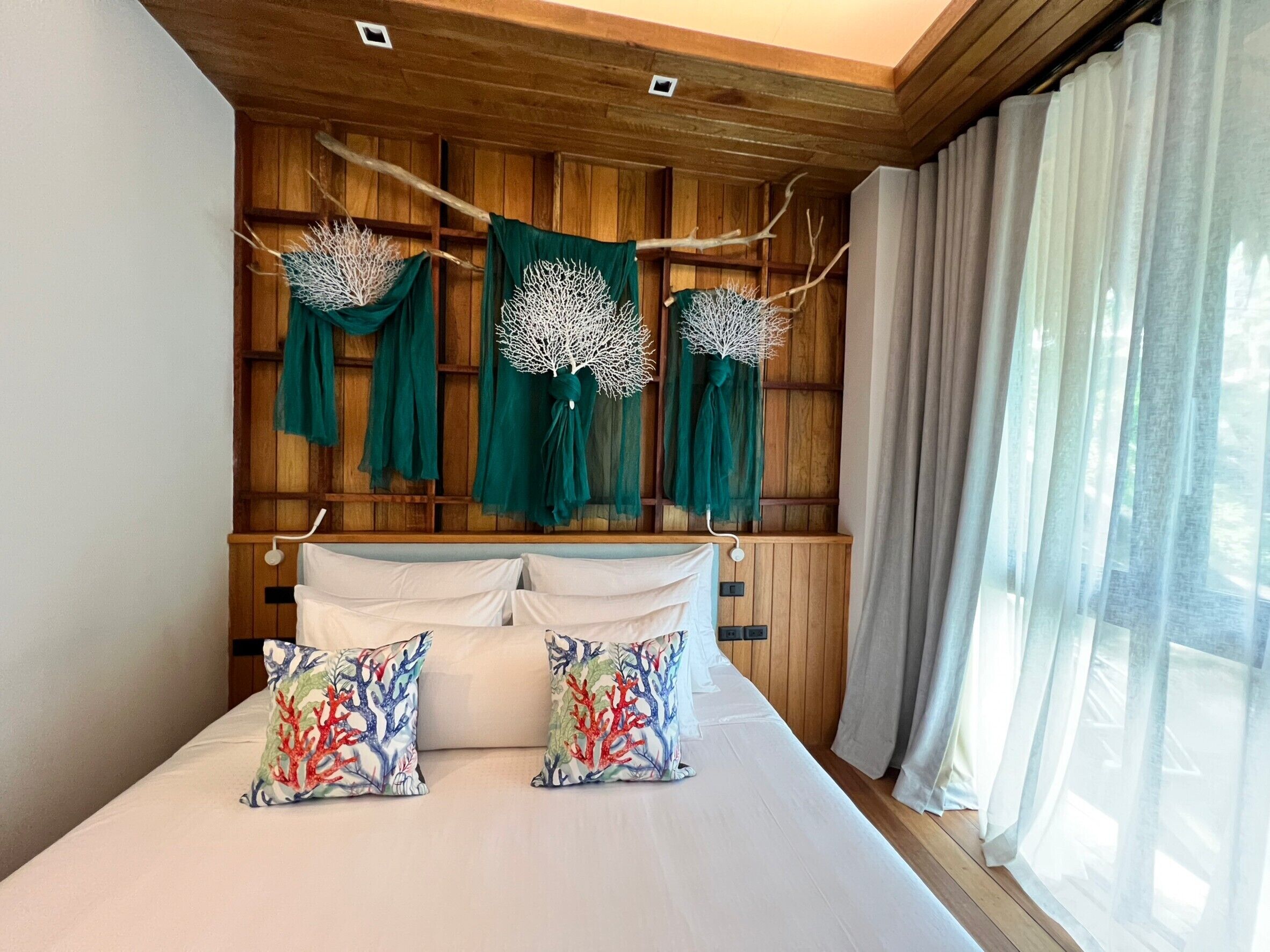 Un dormitorio con cabecera de madera, cama con ropa blanca, ramas decorativas y cortinas de tela verde.