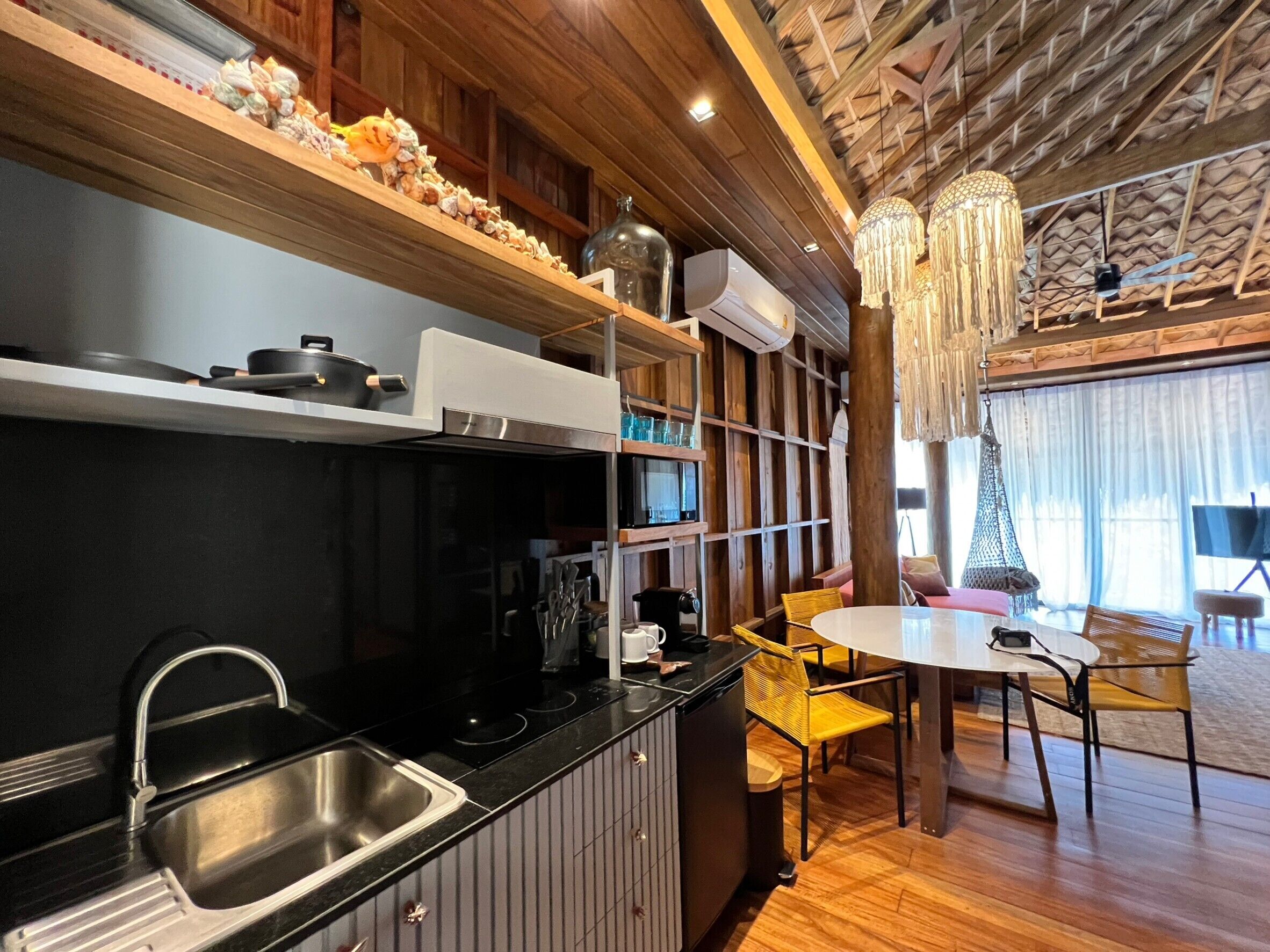 Une cuisine moderne avec un plan de travail noir, un évier en acier inoxydable et des étagères en bois. On y trouve également un coin repas avec une table ronde et des chaises jaunes.