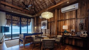 A wooden-floored room with a round table and chairs, a large window with a view of the ocean, and a ceiling fan. - Sealord Naithon Beach Phuket (Sa Khu)