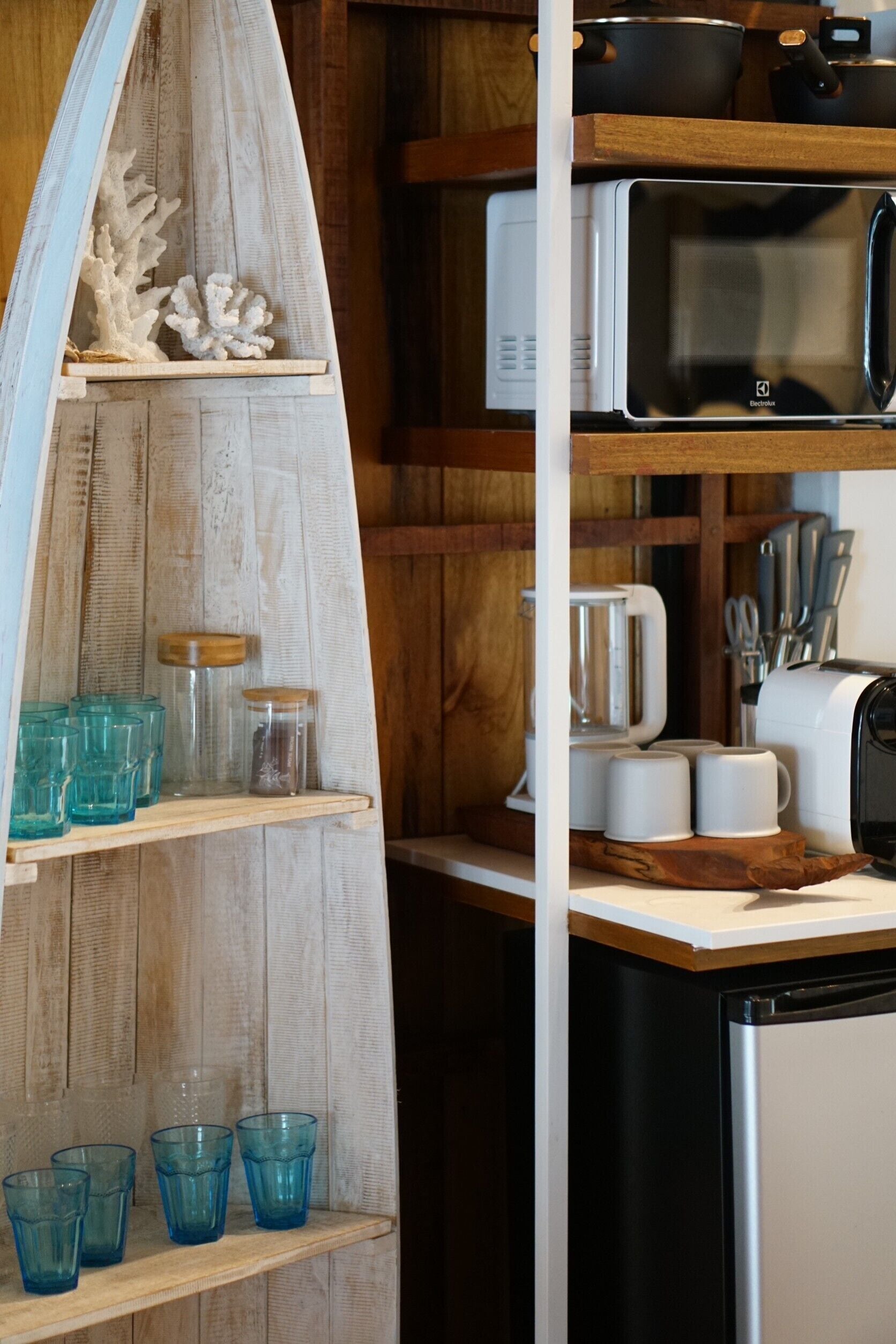 Una cocina con estantes de madera, un microondas, un tostador y varios utensilios de cocina.