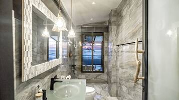 A modern bathroom with a glass-enclosed shower, a marble wall, and a view of the ocean.