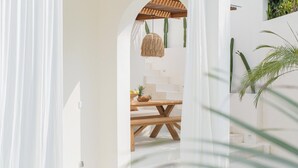 Un espacio interior amplio y luminoso con una mesa y sillas de madera, una lámpara colgante y una escalera que sube a un nivel superior.