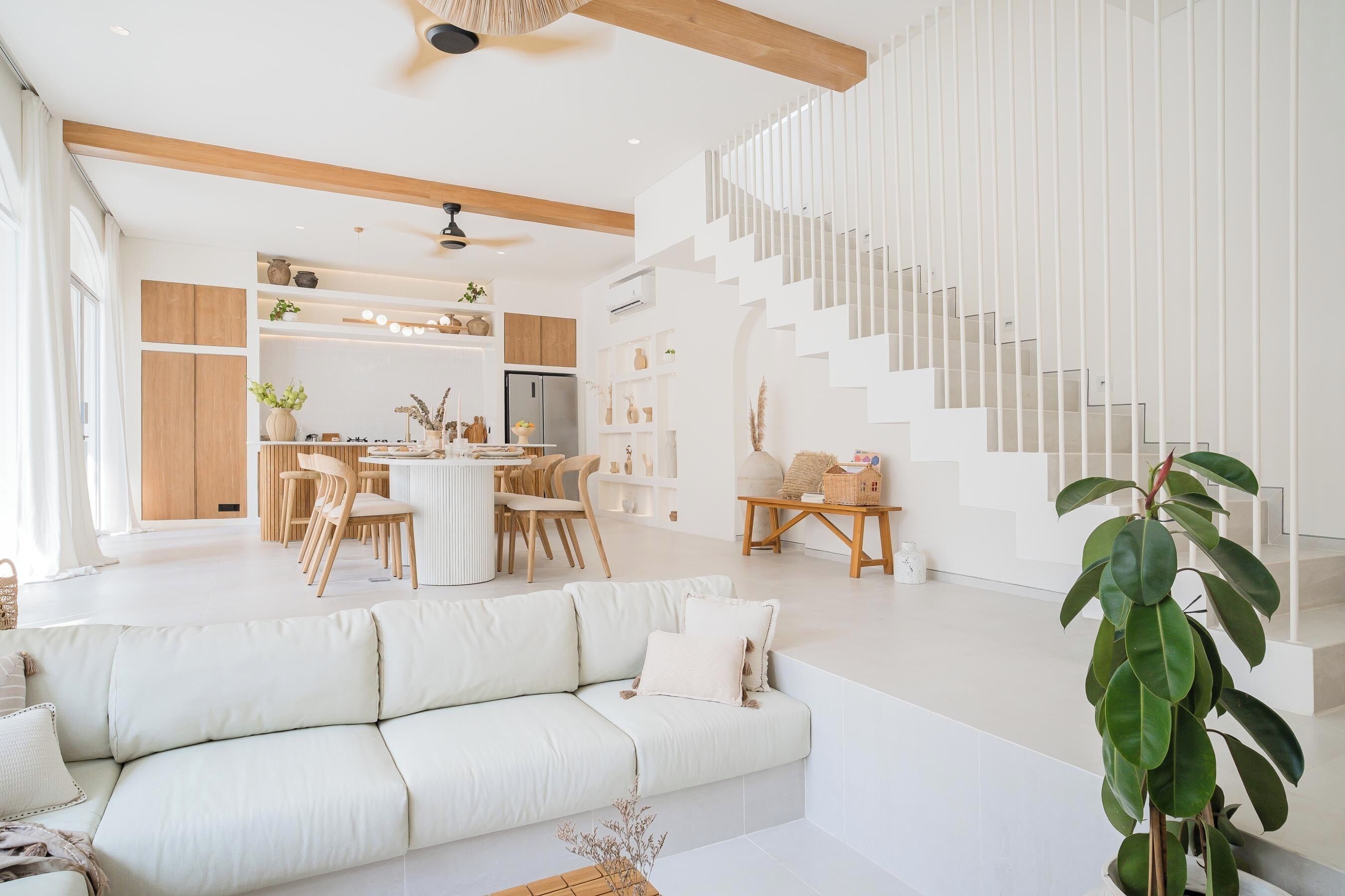 A spacious living area with a white sofa, a dining table with chairs, and a staircase with white railings.