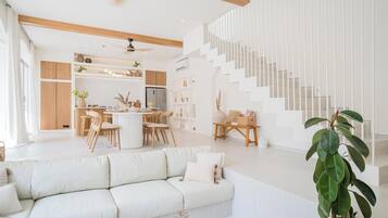 Un vaste espace de vie comprenant un canapé blanc, une table à manger avec des chaises et un escalier doté de rampes blanches.