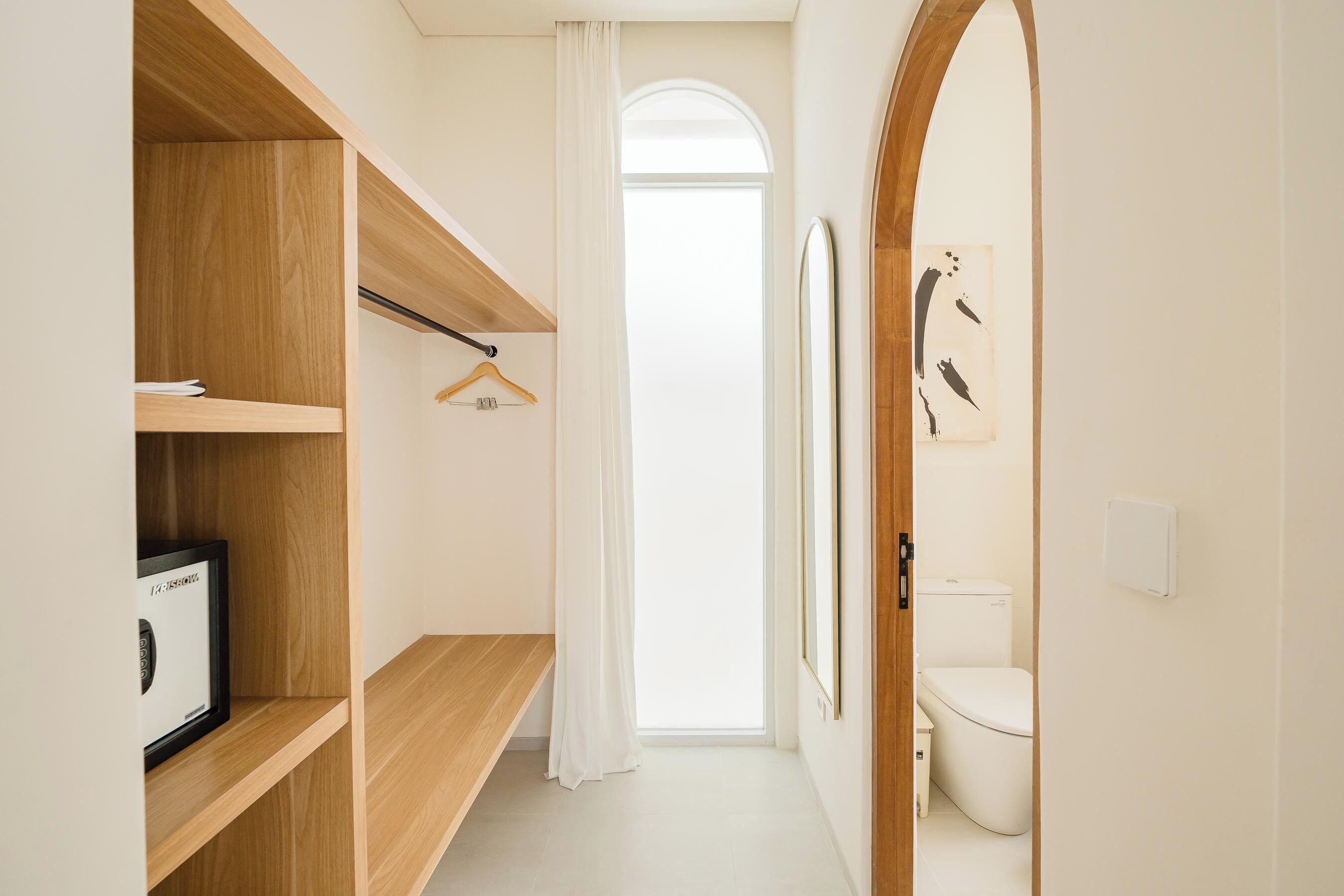 A hallway with wooden shelving, a hanging coat, a framed picture, and a toilet in the background.