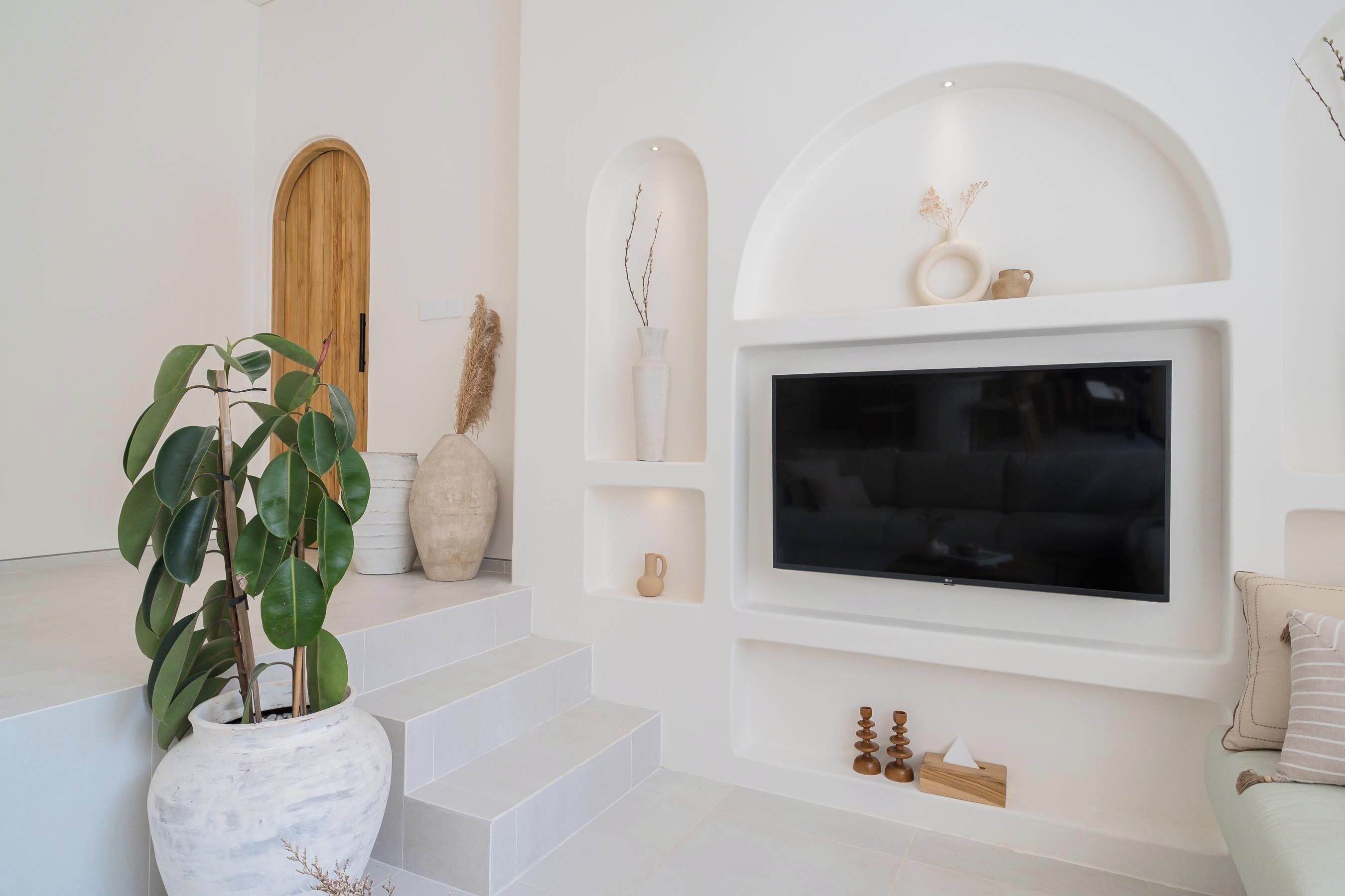 Een moderne woonkamer met een grote flatscreen televisie aan de muur, een trap naar een hoger niveau en een bloempot op de begane grond.
