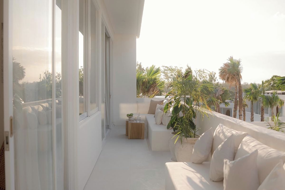A modern balcony with a white sofa, a small wooden table, and a potted plant.