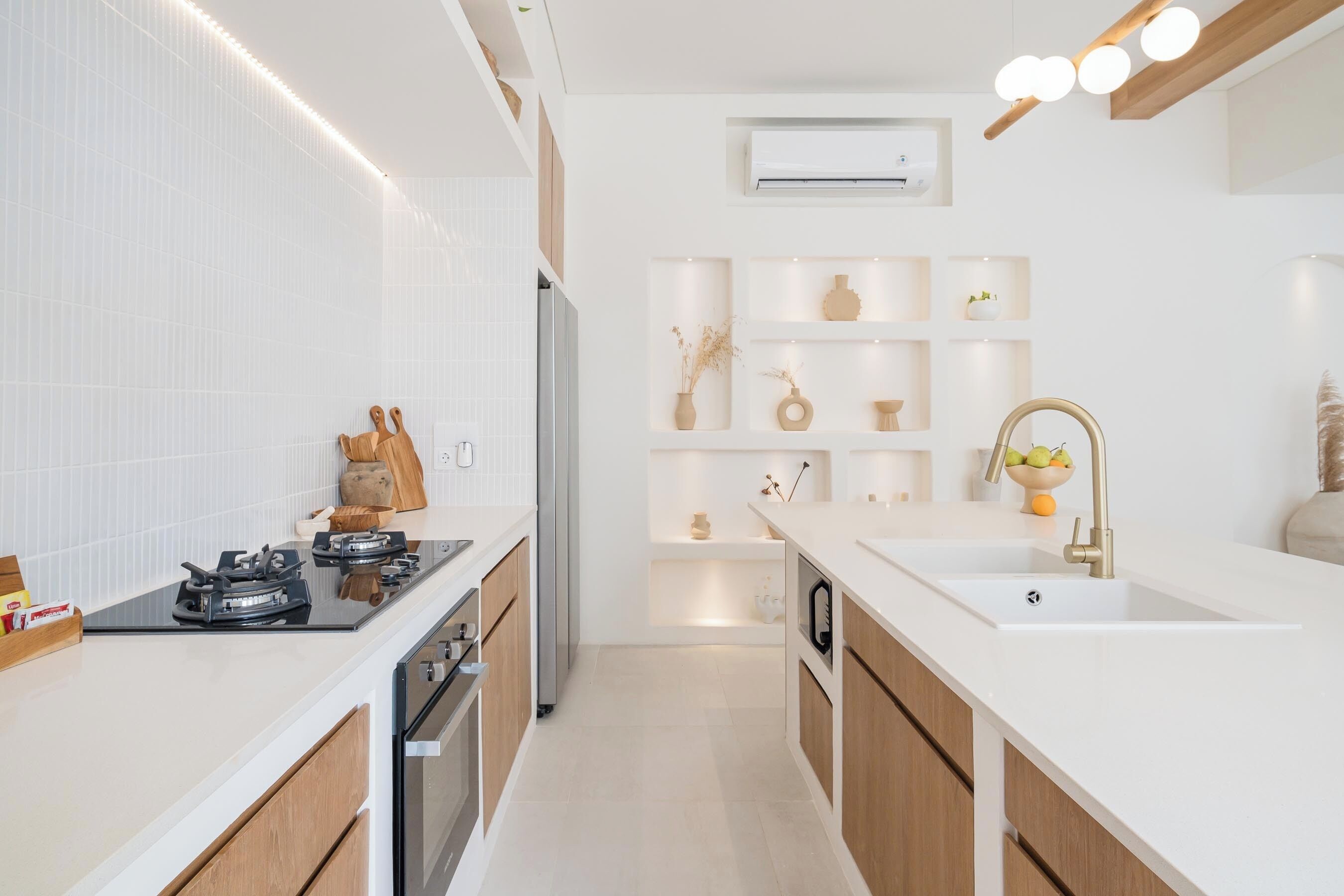 A modern kitchen with white cabinetry, a built-in stove, and a sink. There are shelves with decorative items and a small plant.