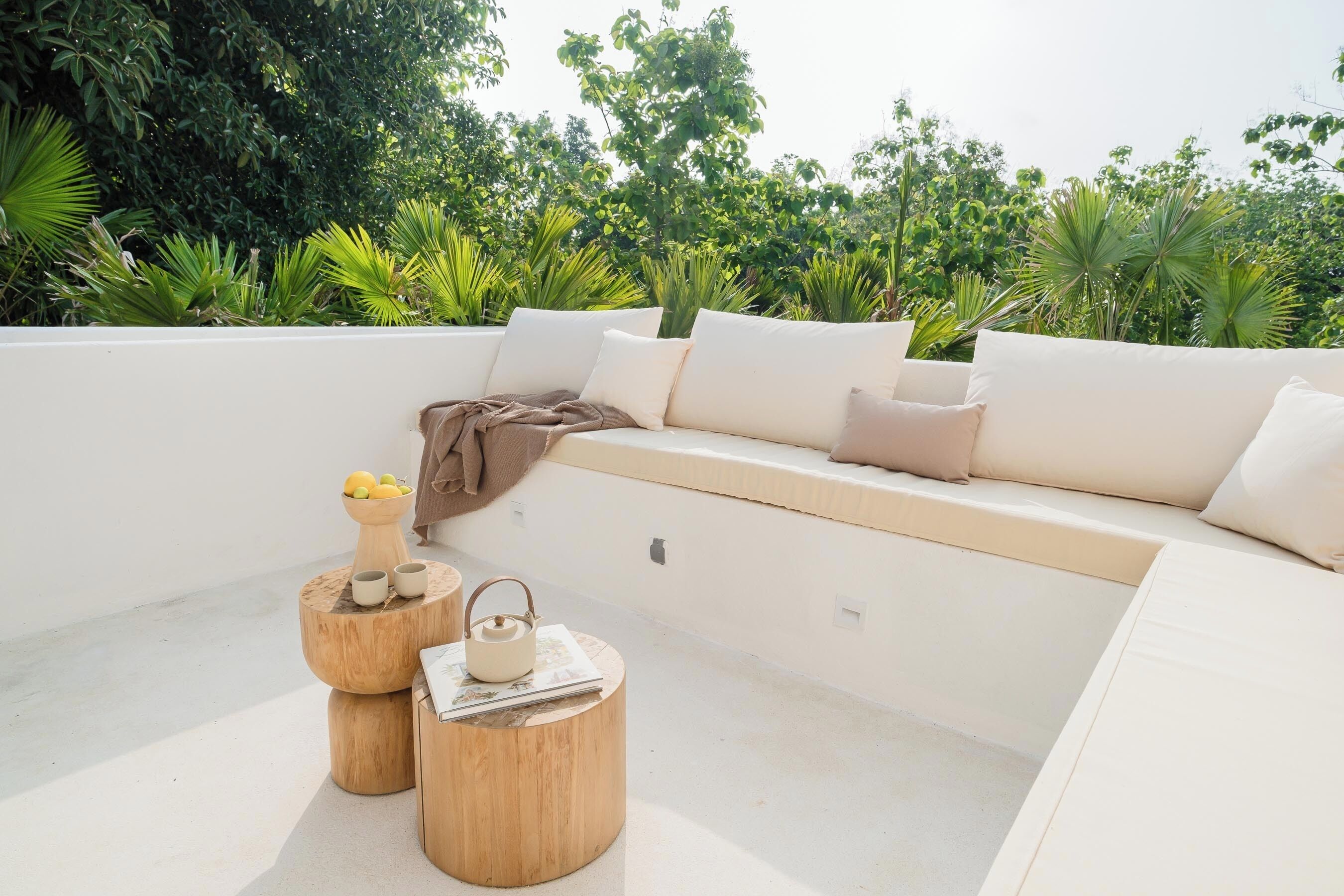 A modern outdoor seating area with a white sofa, cushions, and wooden side tables.
