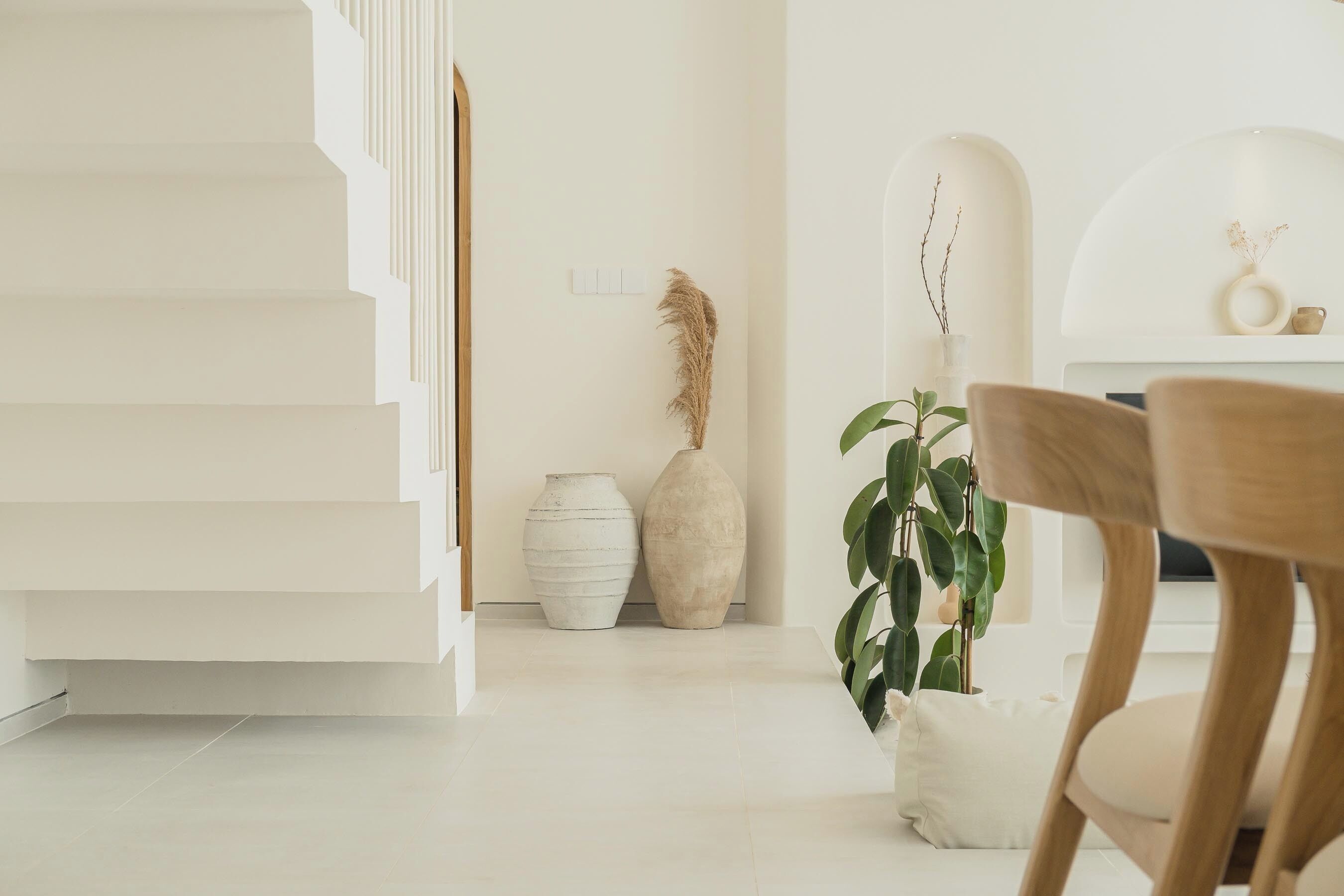 Ein modernes Interieur mit einer Treppe, weißen Wänden und minimalistischer Einrichtung, darunter eine Pflanze und zwei Vasen.