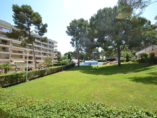 A well-maintained grassy area with a pool, surrounded by trees and a multi-story building with balconies. - Lovely apartment for 4 people with pool, WIFI, A/C, TV and terrace (Salou)