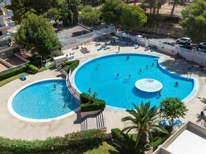 A large outdoor swimming pool with multiple lanes, surrounded by lounge chairs and a small waterfall feature. - Lovely apartment for 4 people with pool, WIFI, A/C, TV and terrace (Salou)