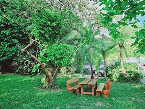 Een weelderige tuin met een houten picknicktafel en bankjes, omgeven door verschillende bomen en groen.