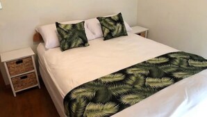 Een net opgemaakt bed met witte lakens en een bedspreide met een patroon van groene palmbladeren.