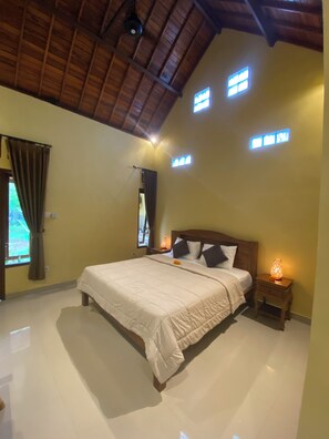 A bedroom with a large bed, a wooden headboard, a nightstand with a lamp, and a window with curtains. - Bali Asli Guest House by EPS (Ubud)