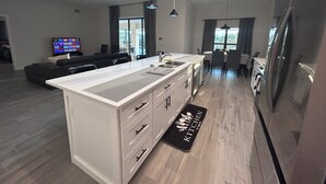 Una cocina moderna con una isla central, un comedor y una sala de estar con televisor.