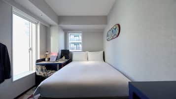 A modern hotel room with a large bed, a desk with a laptop, a chair, and a window with a view of buildings.