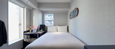 Habitación de hotel moderna con una cama grande, un escritorio con una computadora portátil, una silla y una ventana con vistas a edificios.