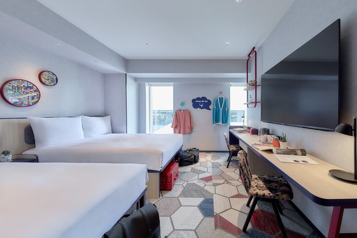 Ett modernt hotellrum med två sängar, ett skrivbord, en platt-TV och ett stort fönster.