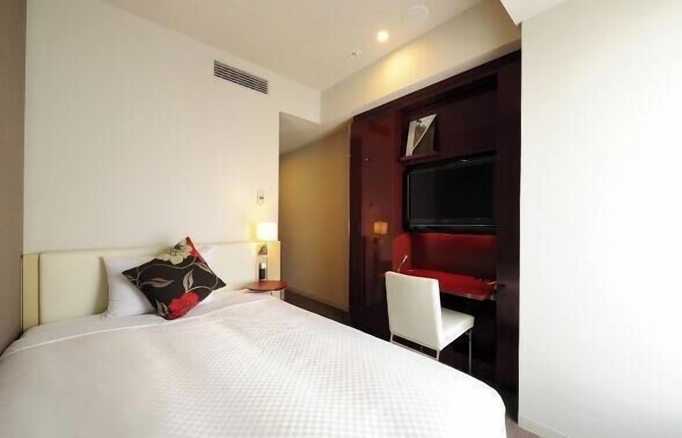 A hotel room with a bed, a desk, a chair, and a TV.