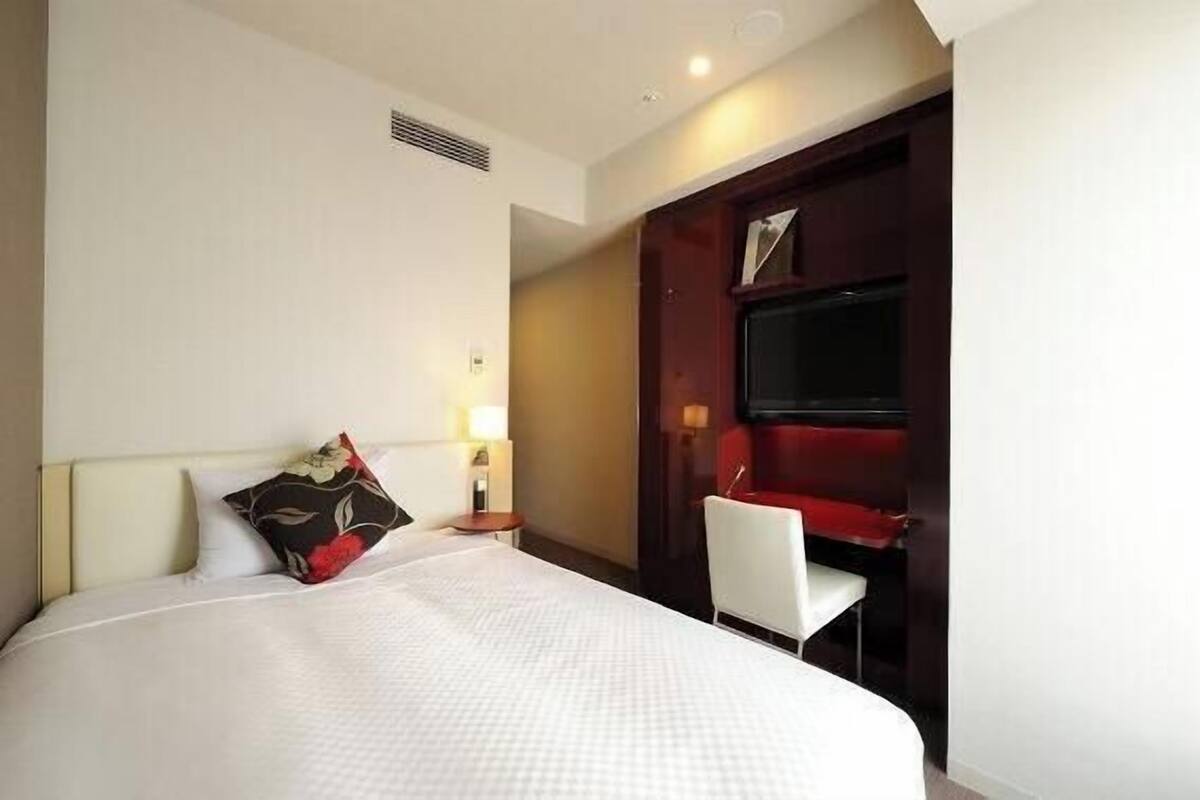 A hotel room with a bed, a desk, a chair, and a TV.