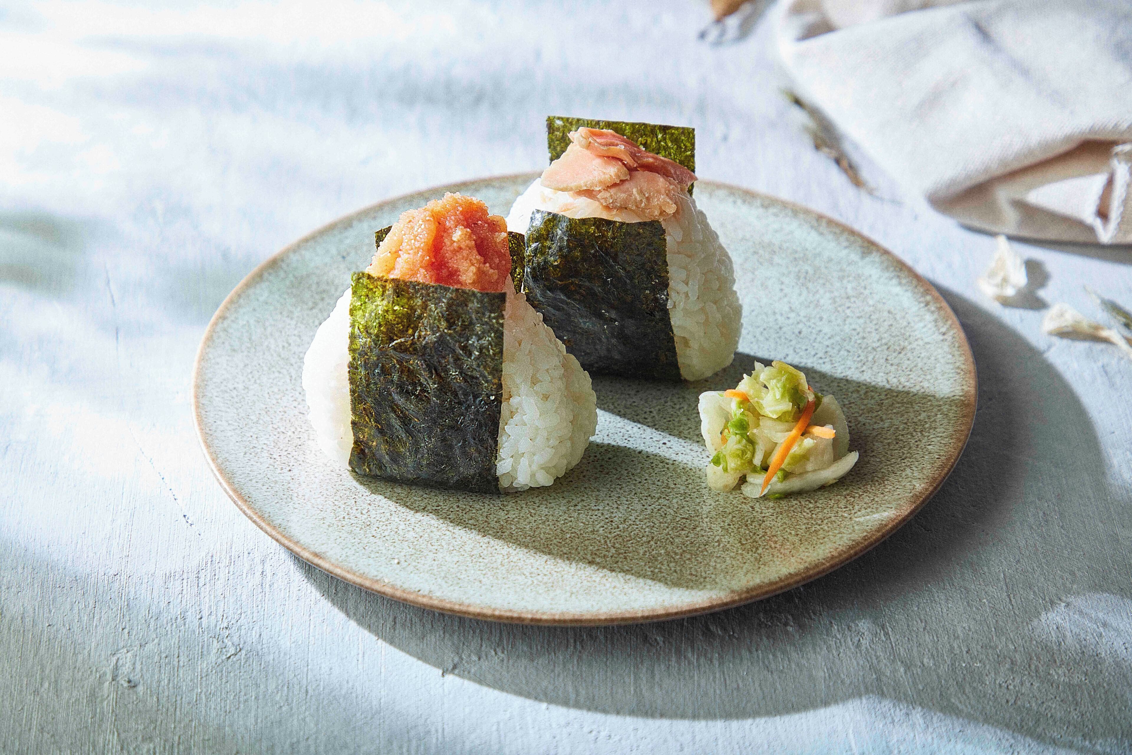 A plate with three sushi pieces and a small salad on a ceramic plate.
