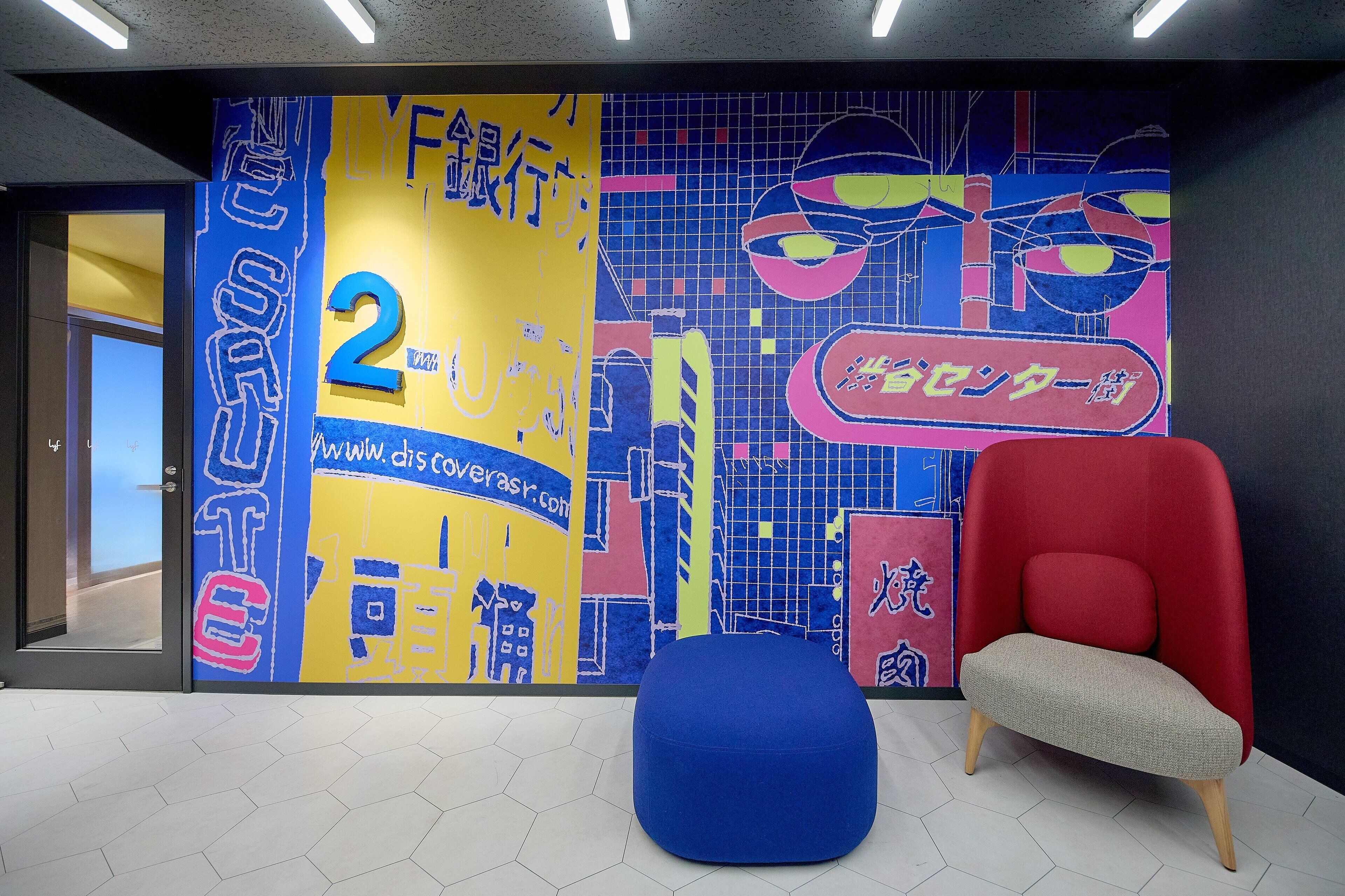 A modern interior with a colorful mural, a red chair, and a blue ottoman.