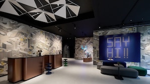 Un espace d’accueil moderne doté d’un plafond au design géométrique, d’un comptoir d’accueil, d’un espace salon et d’un grand écran numérique.