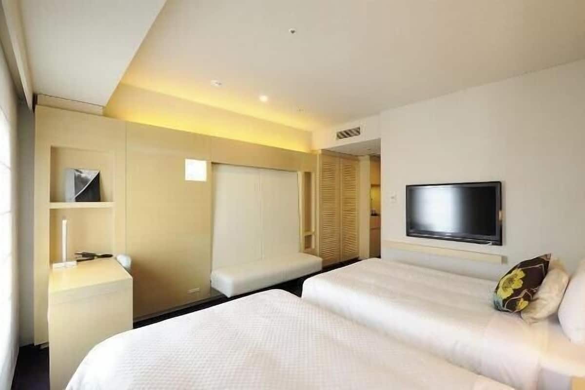 A hotel room with two beds, a flat-screen TV, a bedside table, and a wardrobe.