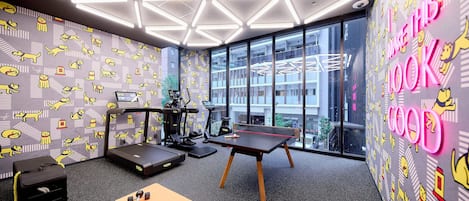 Un gimnasio moderno con equipamiento de ejercicio, un ventanal grande y una pared con personajes de dibujos animados.