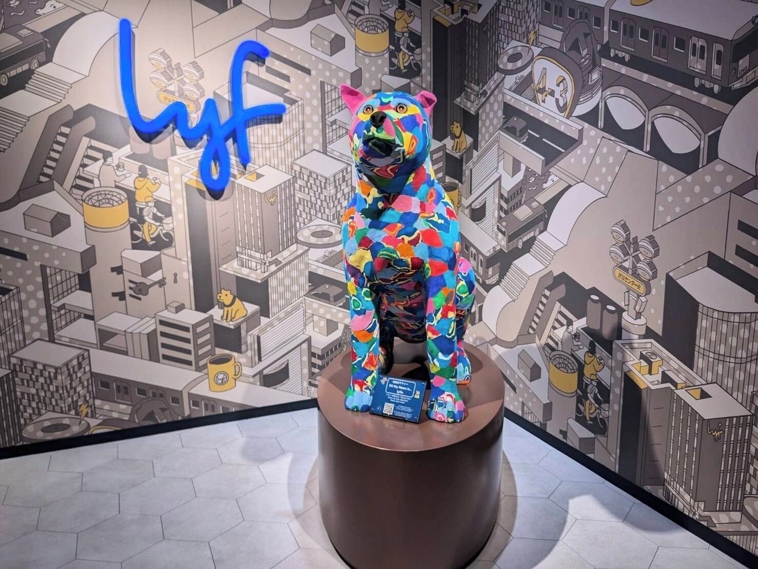 A colorful bear statue on a pedestal with a cityscape mural in the background.