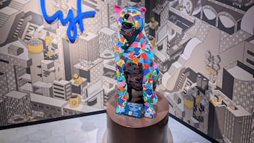 A colorful bear statue on a pedestal with a cityscape mural in the background.