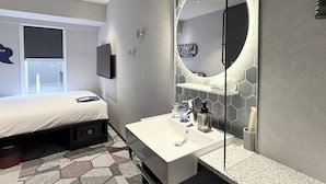 Une chambre d’hôtel moderne avec un grand lit, un lavabo blanc, un miroir et un sol orné d’un motif géométrique.