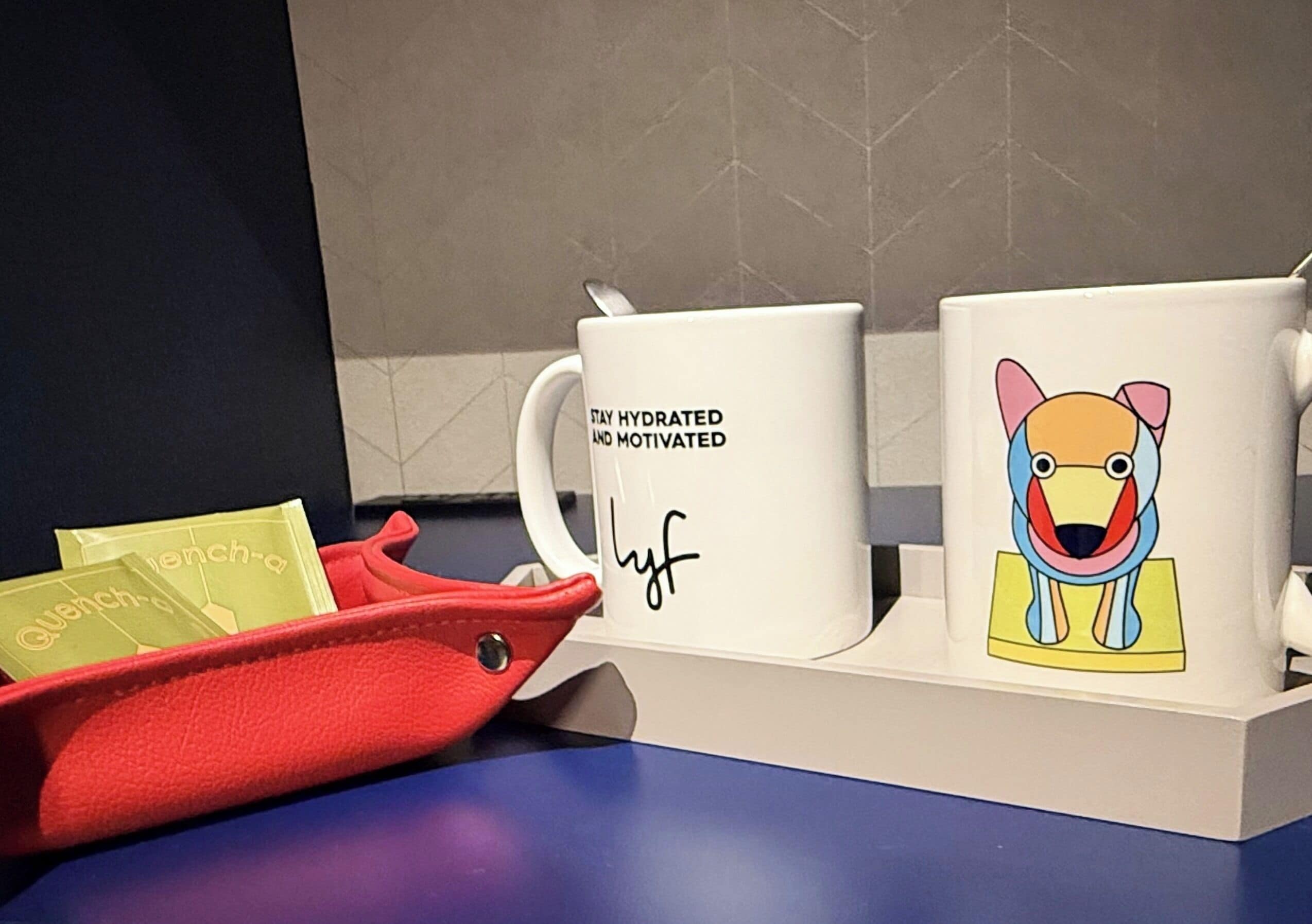 A coffee station with two mugs, one with a dog illustration and text, and another with motivational writing.