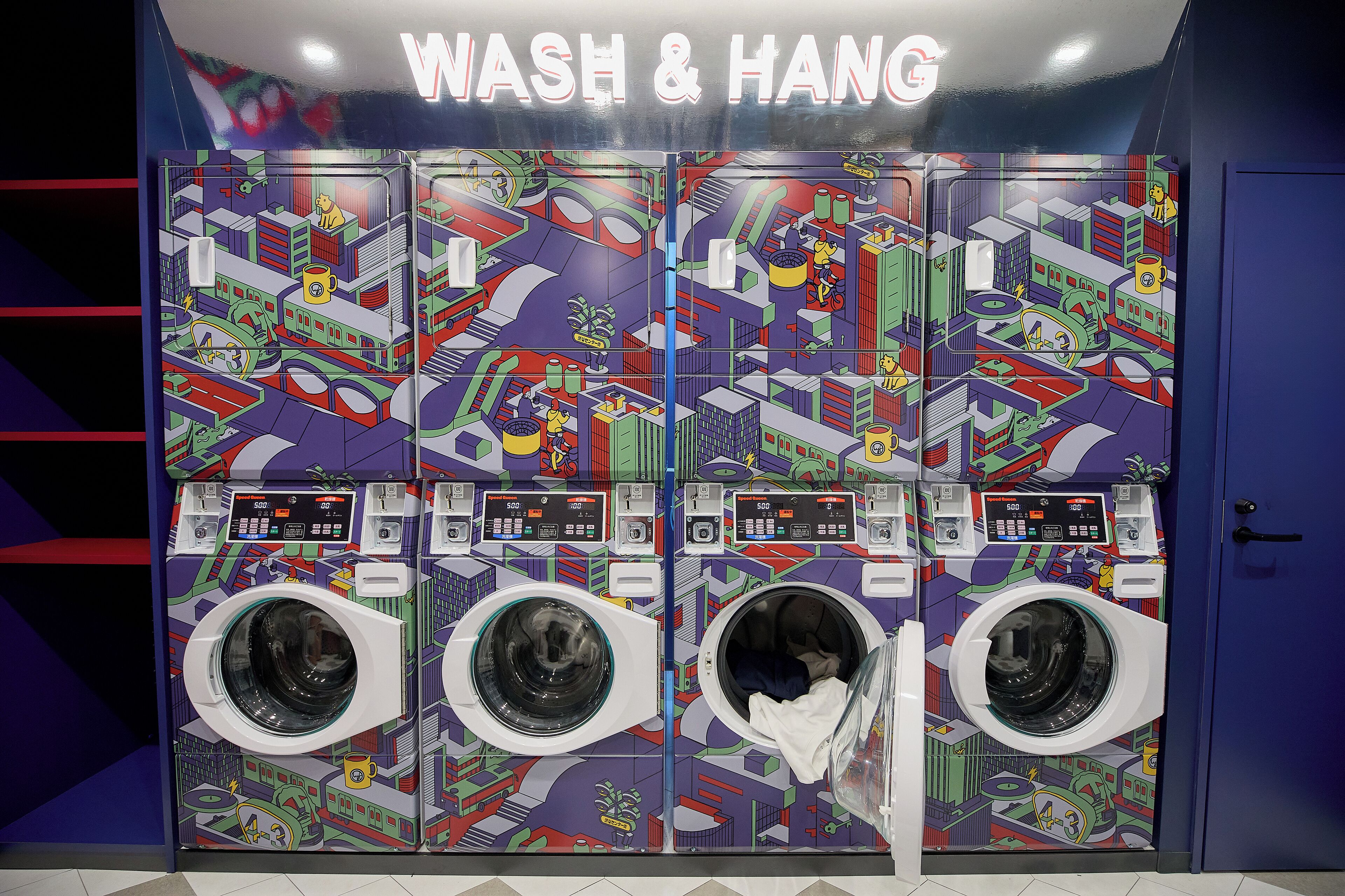 A public wash and dry facility with multiple washing machines and dryers, featuring a colorful, geometric mural design.