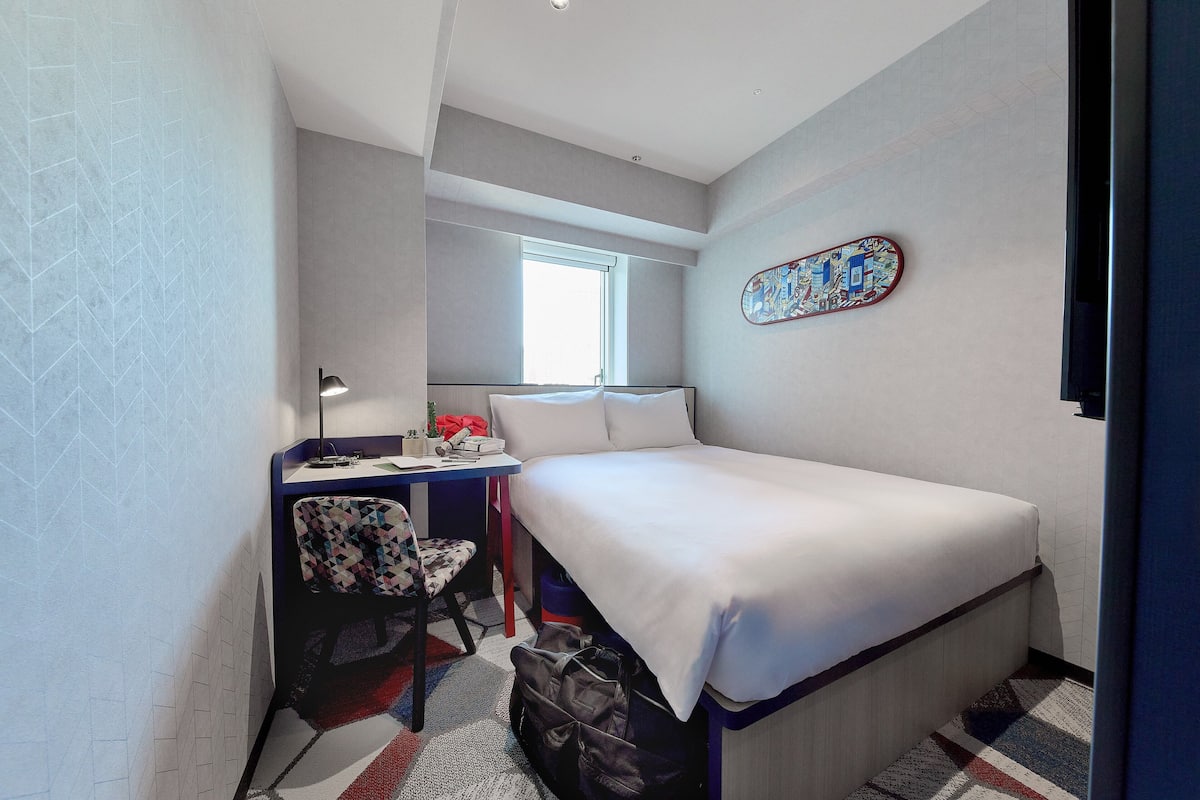Ett litet hotellrum med en säng, ett skrivbord och en stol.