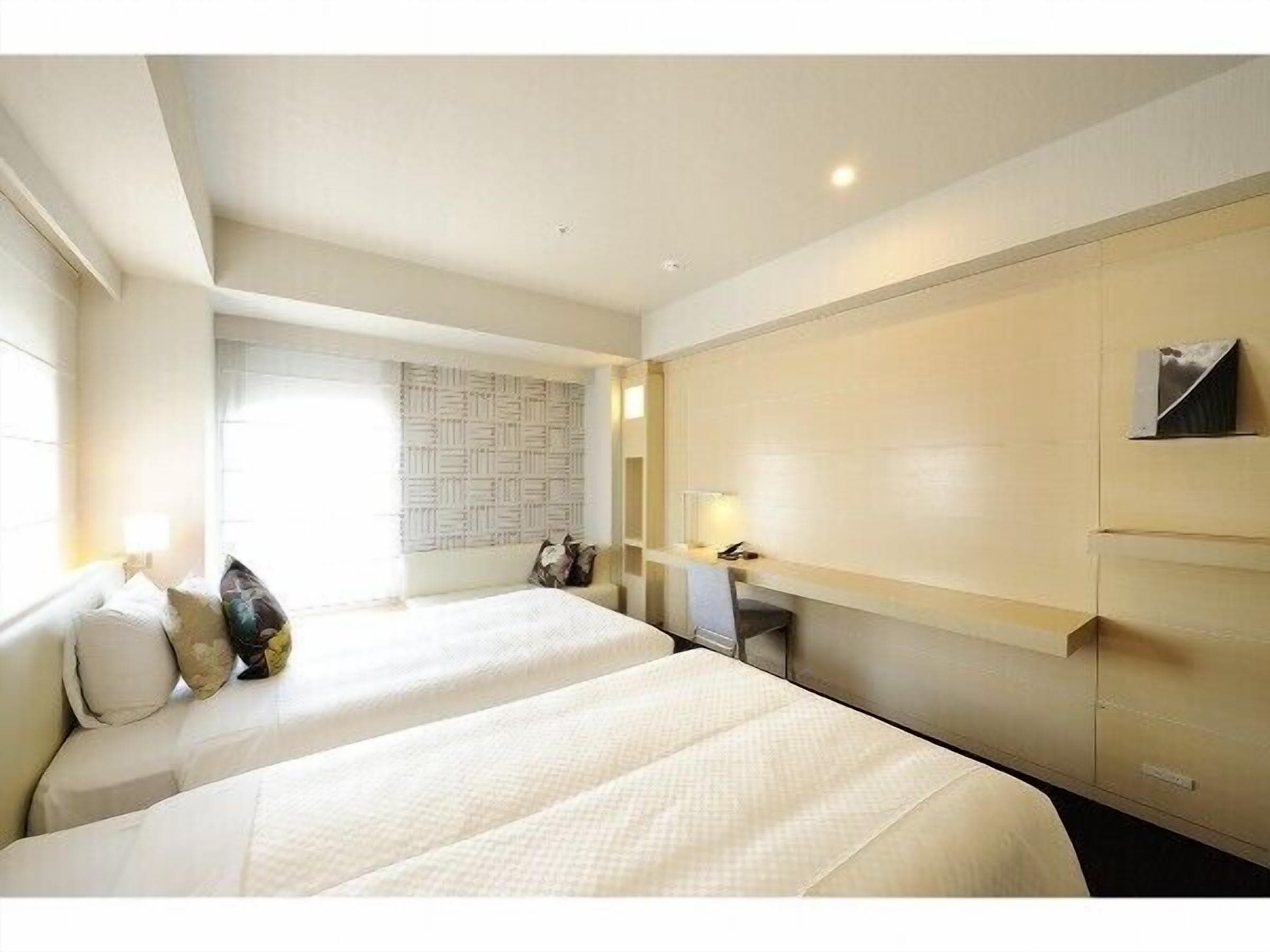 Une chambre d’hôtel avec deux lits, un bureau, une chaise, une lampe et un téléviseur fixé au mur.