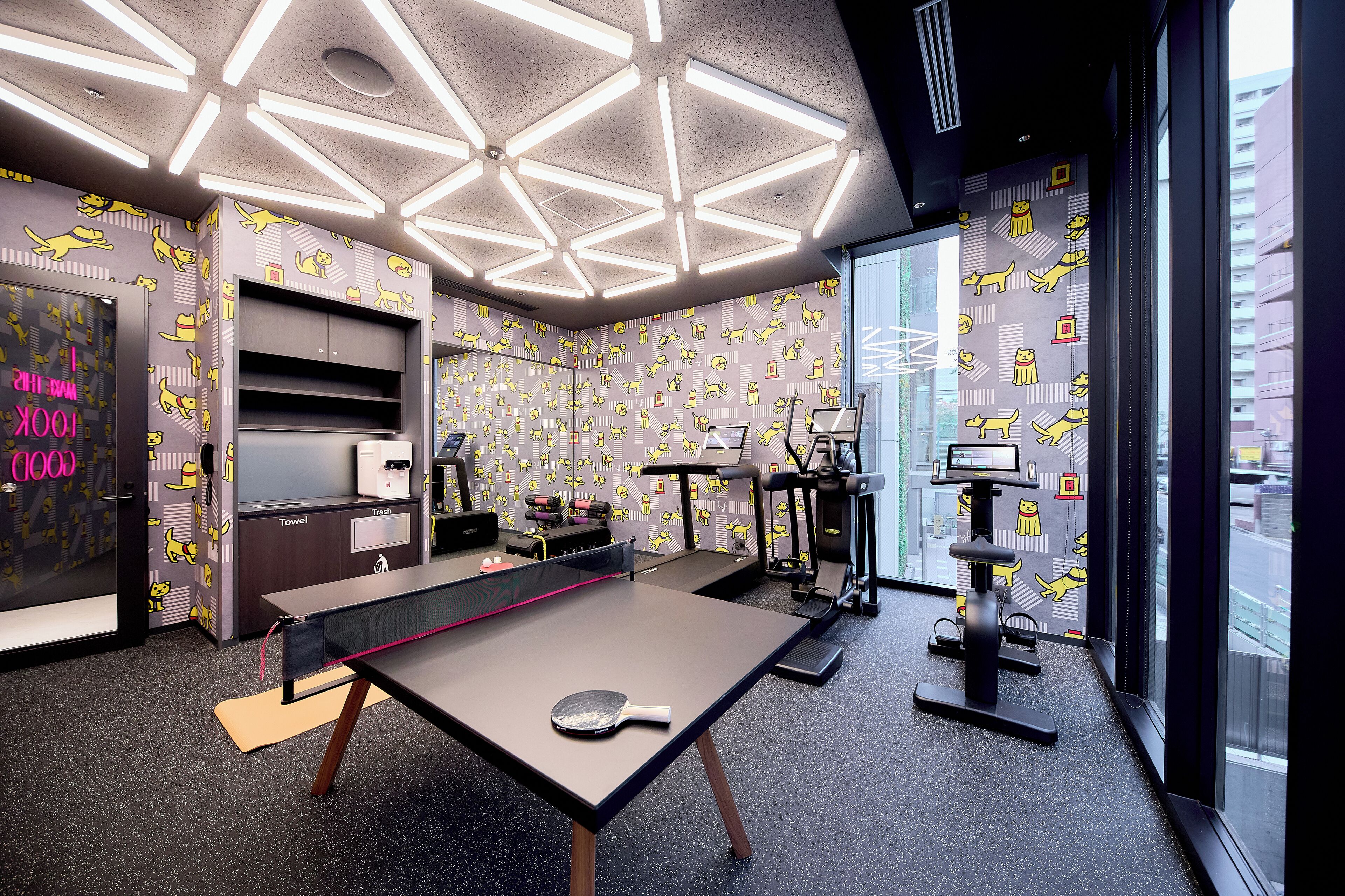 A modern room with a ping pong table, exercise equipment, and a large window offering a city view.