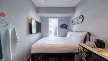 A modern hotel room with a bed, desk, and a view of the city through the window.